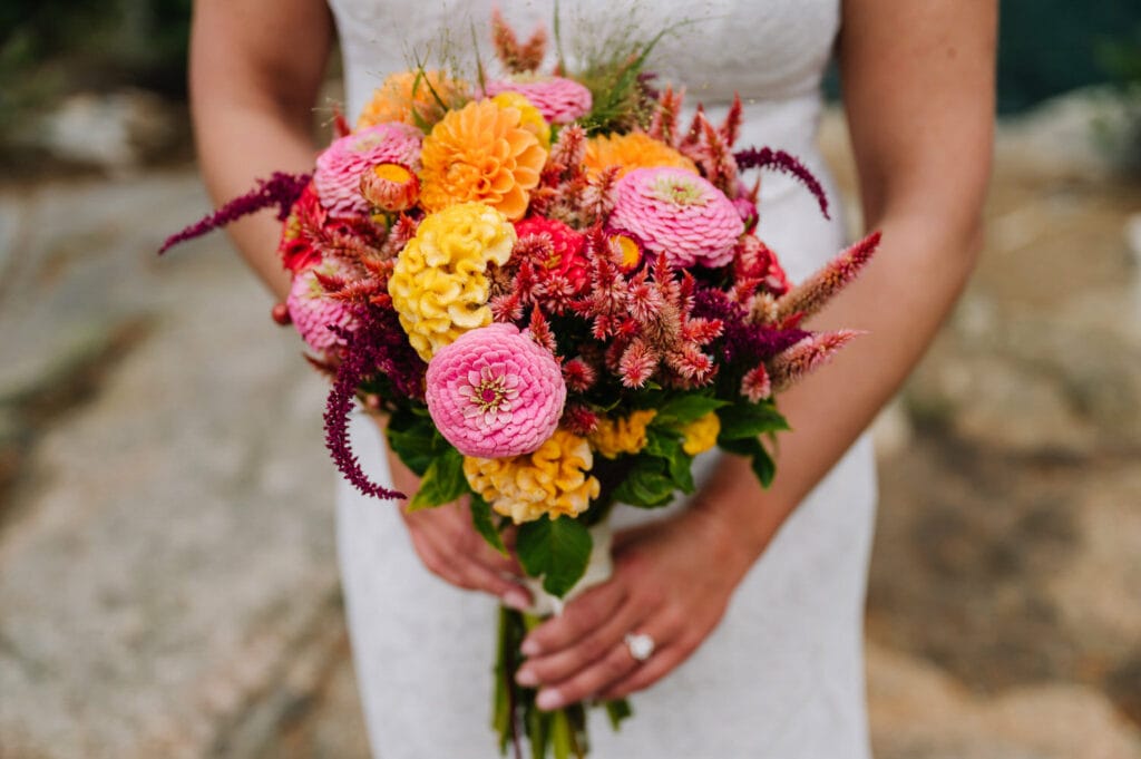 Bride holds a Leave No Trace aware bouquet of yellow, pink and red flowers during her Stanley elopement.
