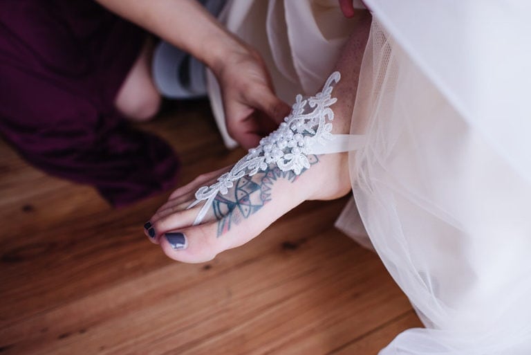Bride puts on her barefoot wedding sandals during a wedding day at Moonridge Cabin in McCall, Idaho.
