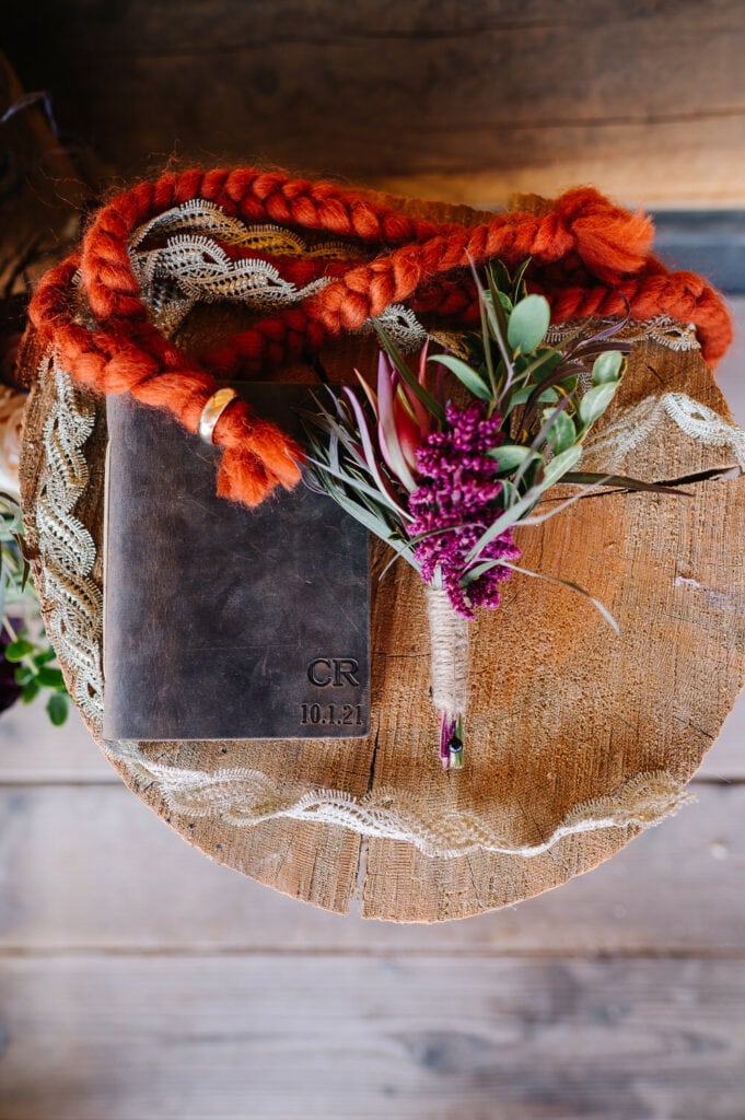 Elopement details laying on a log. Details include a leather vow book, boutonniere, and orange cord for a handfasting ceremony.