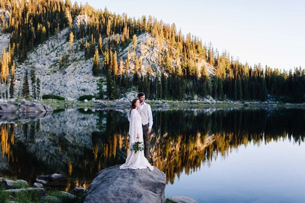 Louie Lake is an adventurous wedding venue in McCall Idaho. Couple standing on rock with mountain reflecting on lake water.