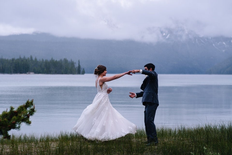Wedding couple dances in front of the sawtooth mountains during their Bride and groom embrace with snow falling around them at their Redfish Lake Lodge Wedding in Stanley, Idaho.