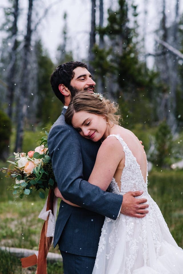Bride and groom embrace with snow falling around them at their Redfish Lake Lodge Wedding in Stanley, Idaho.