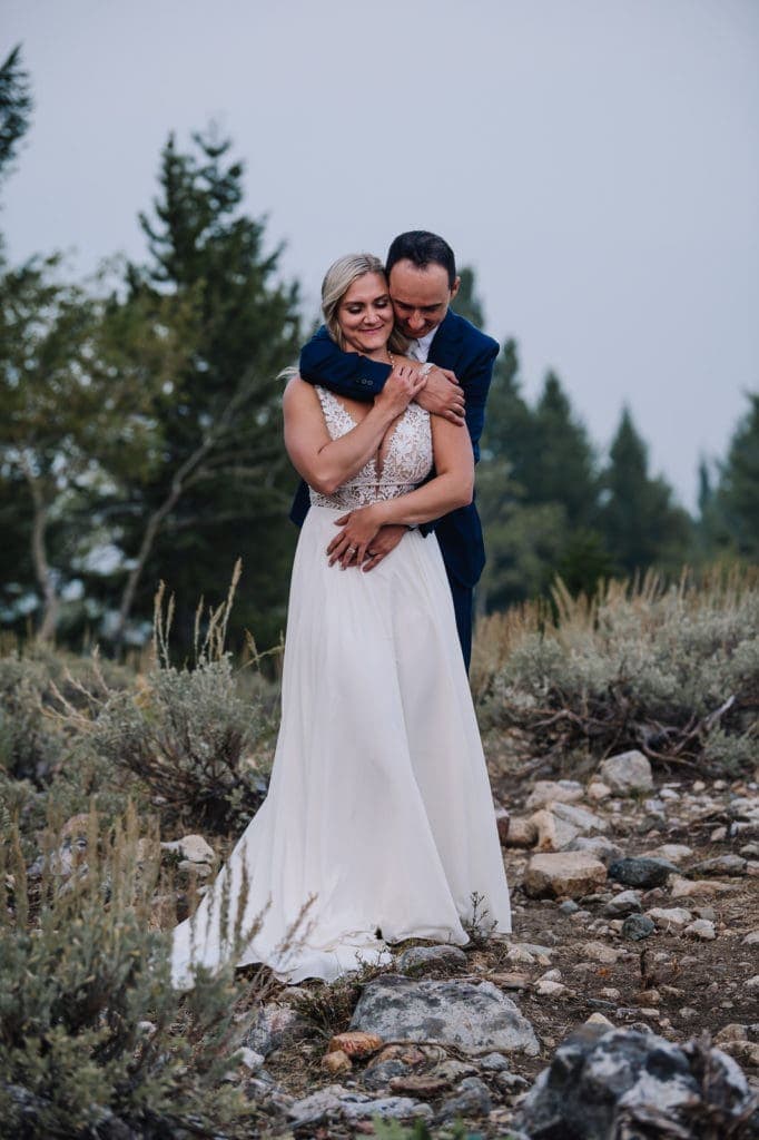 Eloping coupe embraces with pine trees and sagebrush behind them during their McCall, Idaho elopement.