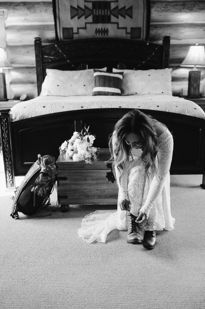 A bride ties her hiking boot on the foot of a bed during her elopement.