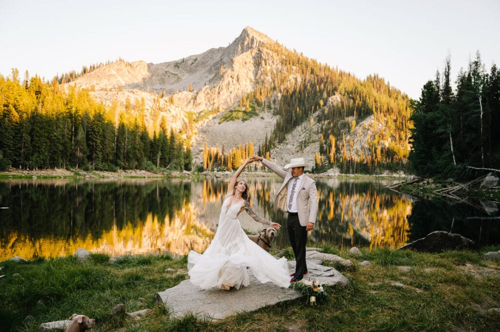 Now that you know a little about the area, let’s jump into how to elope in McCall, Idaho.
A groom and bride dance on a flat rock in front of an alpine lake in McCall, Idaho. This couple eloped at sunset with their two dogs.