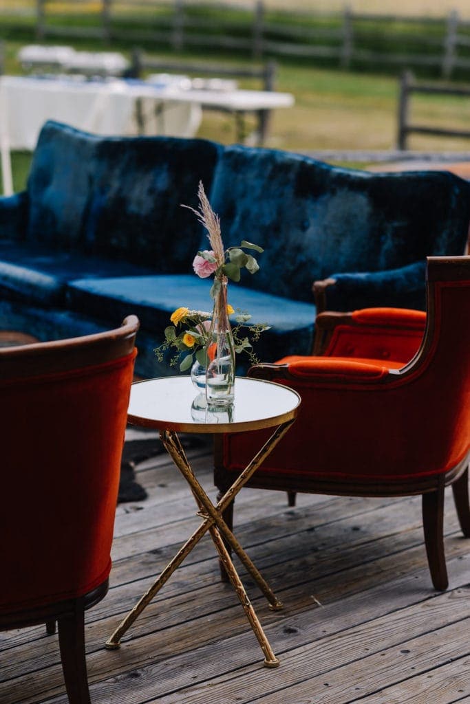Orange velvet chairs and a blue velvet couch sit on a deck. Reception space decoration ideas. 