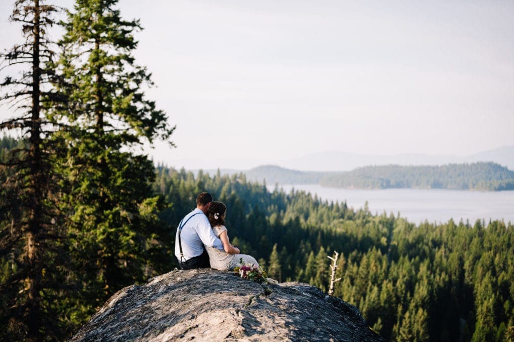 Bride and groom sit together on a rock overlooking Payette Lake. This couple planned a sunrise hike as part of their McCall, Idaho wedding celebration.