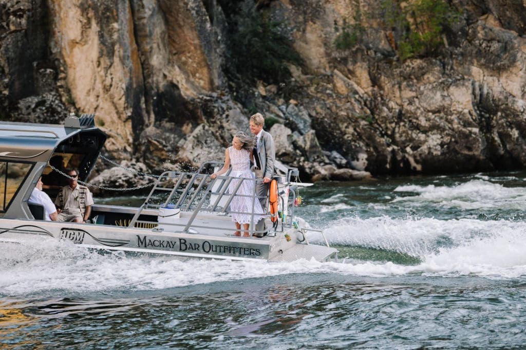 Bride and groom stand on the back of a moving jet boat during their elopement on the Salmon River. Mackay Bar is one of the best places to elope in Idaho.