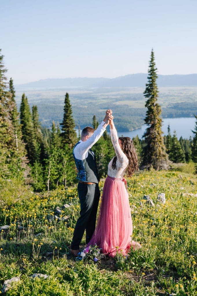 Couple celebrates after their elopement ceremony in the mountains outside of McCall, Idaho. Couple is standing on an open ridge with mountains and a lake behind them. Bride is wearing a pink tulle skirt and bodysuit from Sweet Caroline Styles.