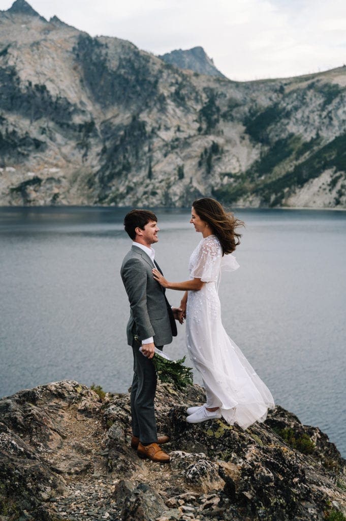 Eloping couple laughs together while the wind tugs at their hair and cloths. Couple is standing on a rocky point overlooking an alpine Lake in Stanley, Idaho. Idaho is one of the easiest states to get married in.