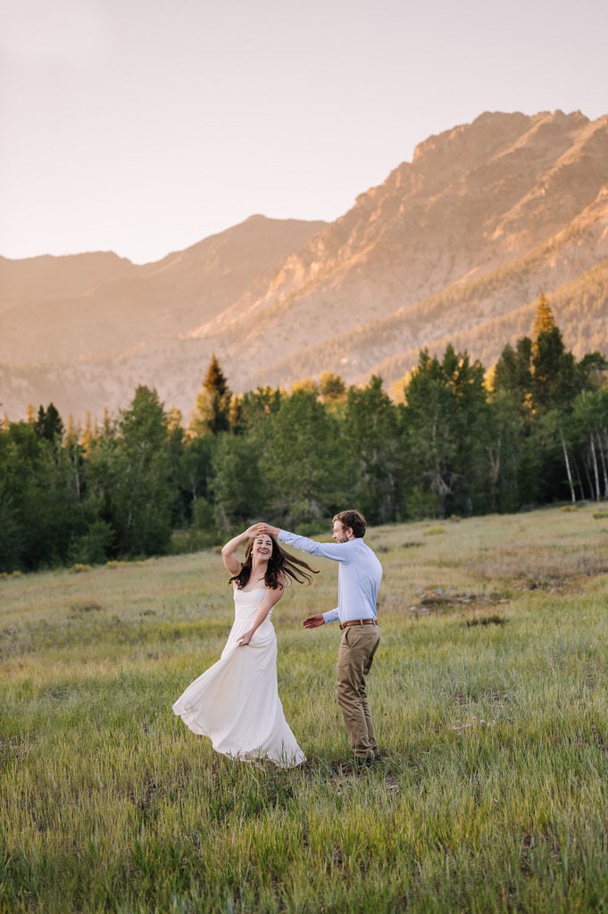 Bride and groom dance during their Sun Valley elopement. The couple is dancing in a meadow and the setting sun is casting a yellow alpenglow on the mountains behind them. 