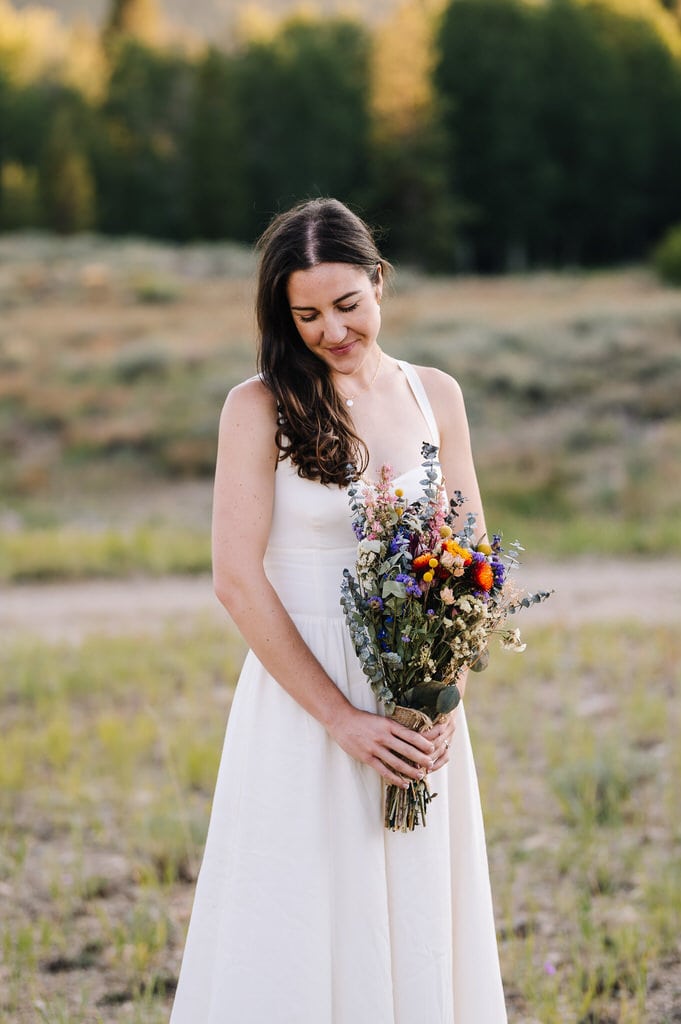 Bride holds a bouquet of dried strawflowers and is wearing a cream colored wedding dress. 