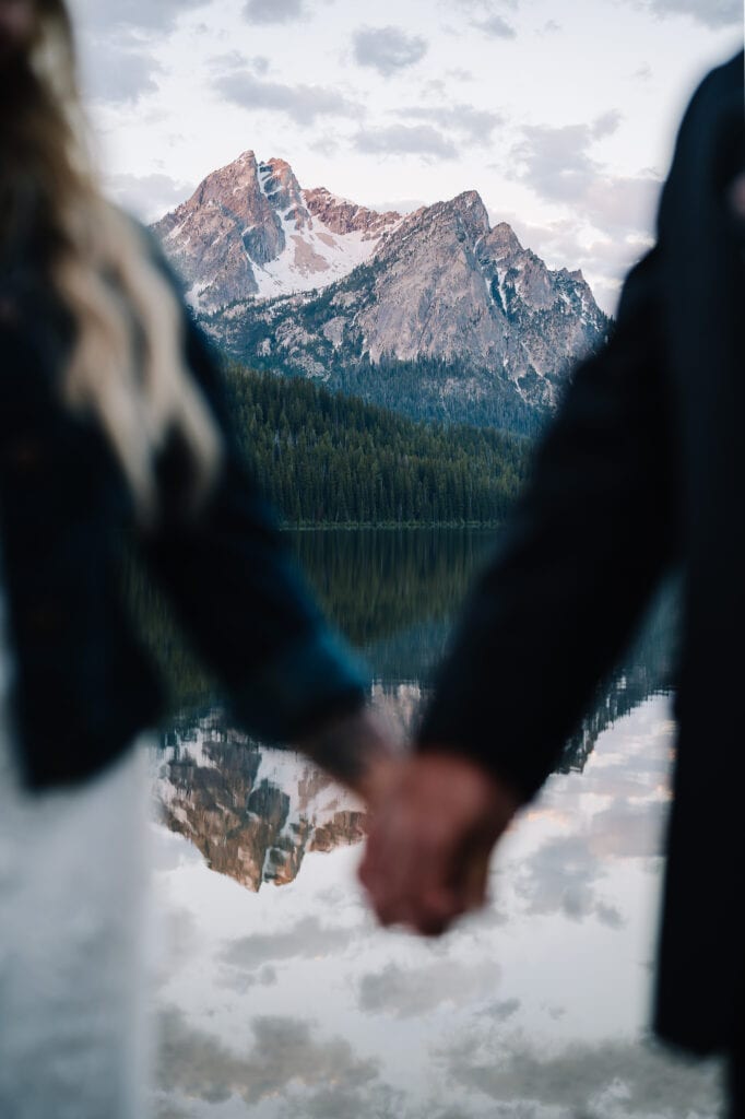 Image of a mountain lake framed by a couple holding hands. This couple chose Stanley, Idaho has the location for their Idaho elopement package(s).