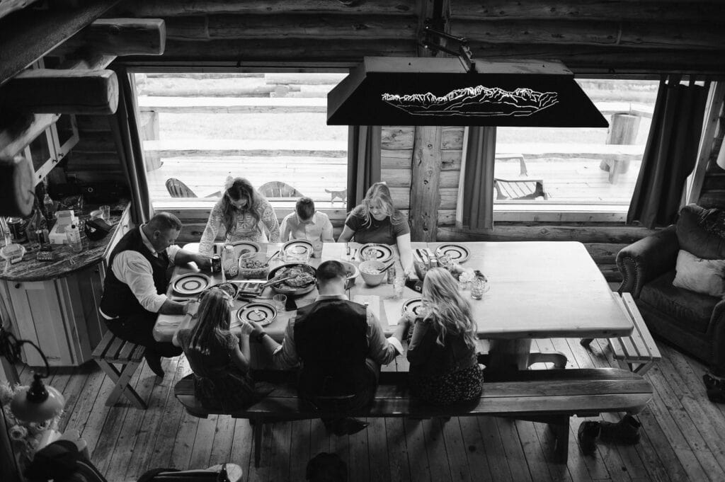A newly married couple shares a dinner blessing with their family. This couple planned an intimate wedding experience for their guests that included a ceremony in the Idaho mountains and a home cooked meal at a rental cabin.