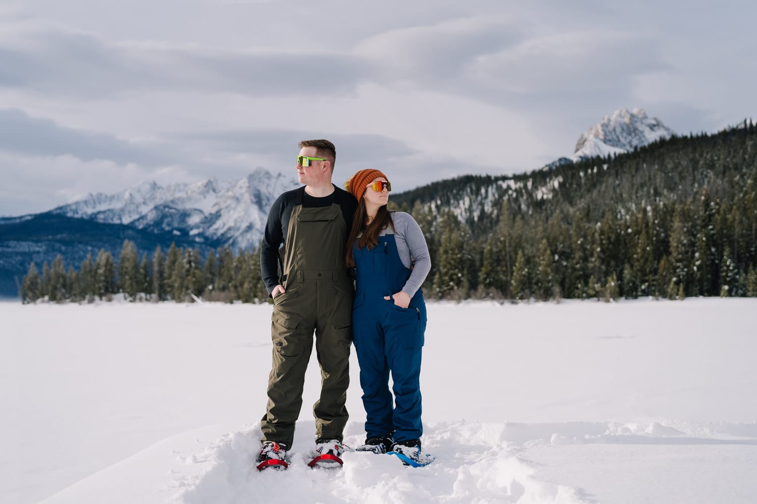 A couple Stands together on the Redfish Lake Lodge dock. The couple snowshoed into the lake for their engagement session. 