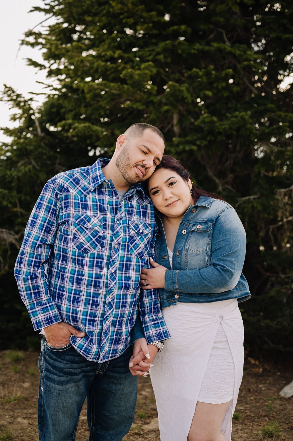 A woman leans on her partner and makes eye contact with the camera. The couple is wearing blue toned clothing for their engagement session in cascade, Idaho.