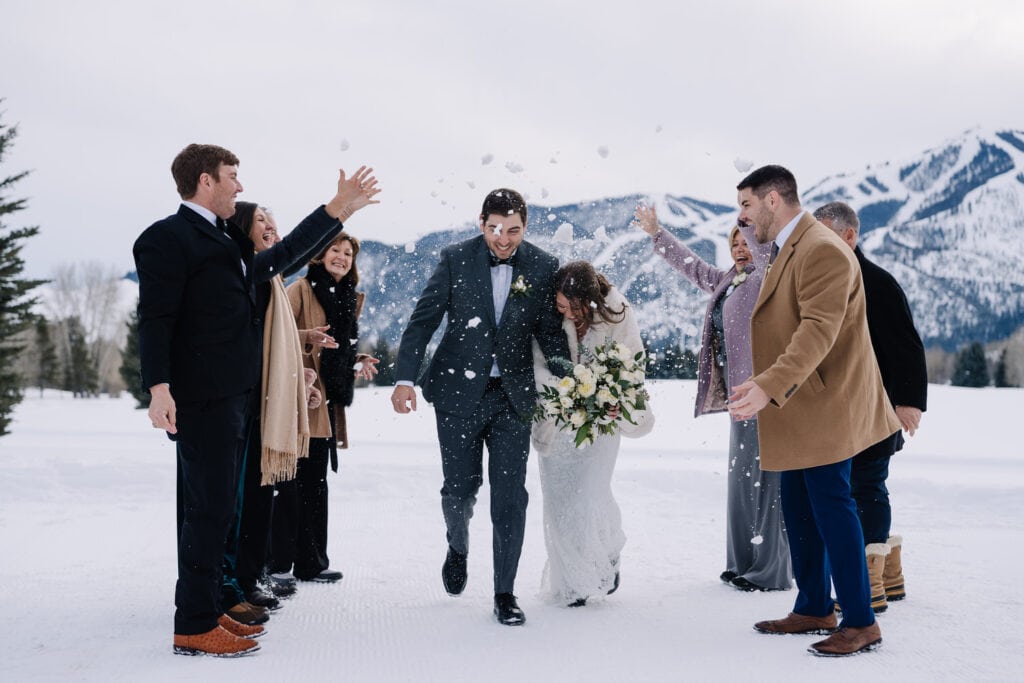 Wedding guests throw snow over a bride and groom as they walk down the aisle. Bold Mountain is in the background. This couple eloped with their family in Sun Valley, Idaho.
