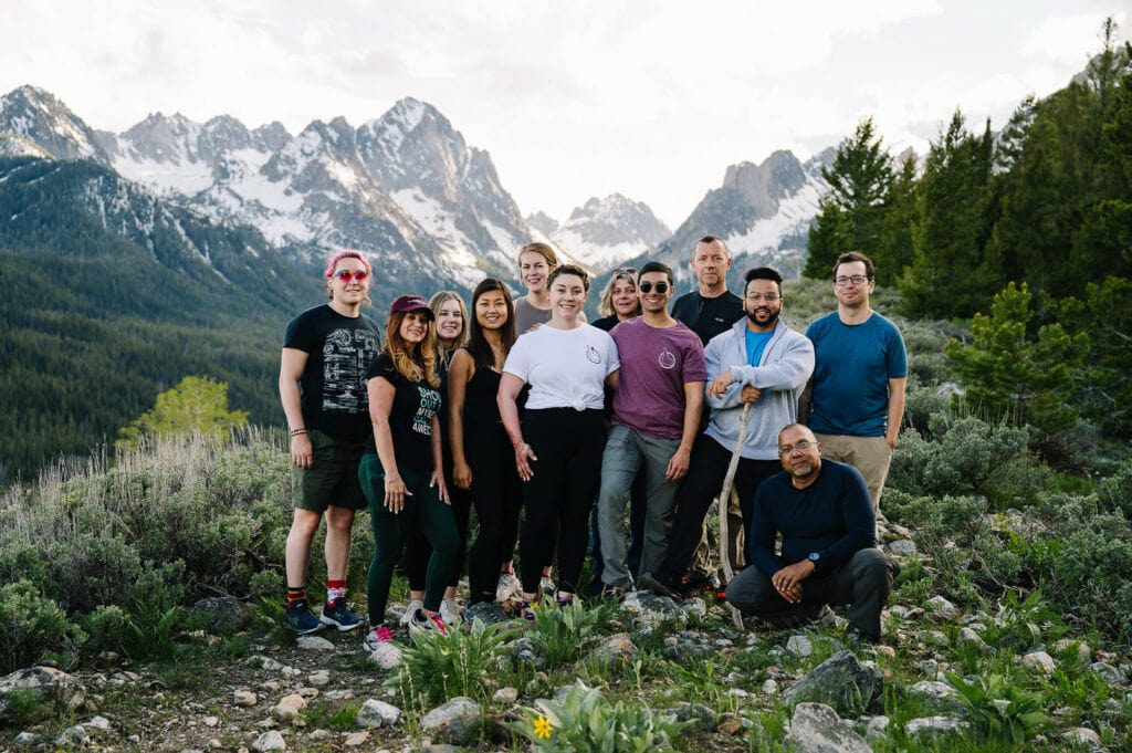 A couple stands with their wedding guests on a ridge. There are mountains behind the group. This eloping couple chose a photo location with a small hike.
