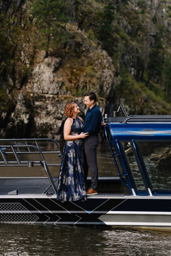 A wedding couple stands on a blue jet boat during their elopement. The bride is wearing a blue dress and the couple is smiling at each other.