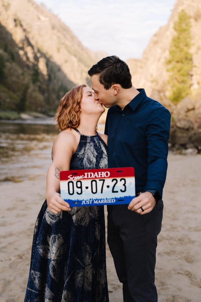 A couple holds out a wedding sign with their custom elopement details. The sign is made to look like an Idaho license plate.